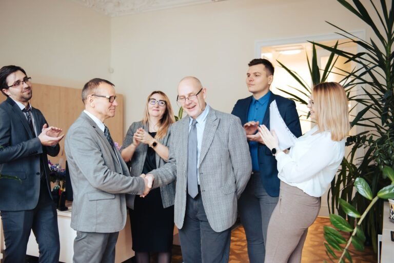Partners shaking hands while colleagues clap